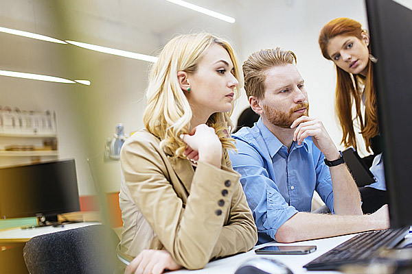 Zwei Frauen und ein Mann in geschäftlicher Kleidung schauen zusammen auf einen Computerbildschirm