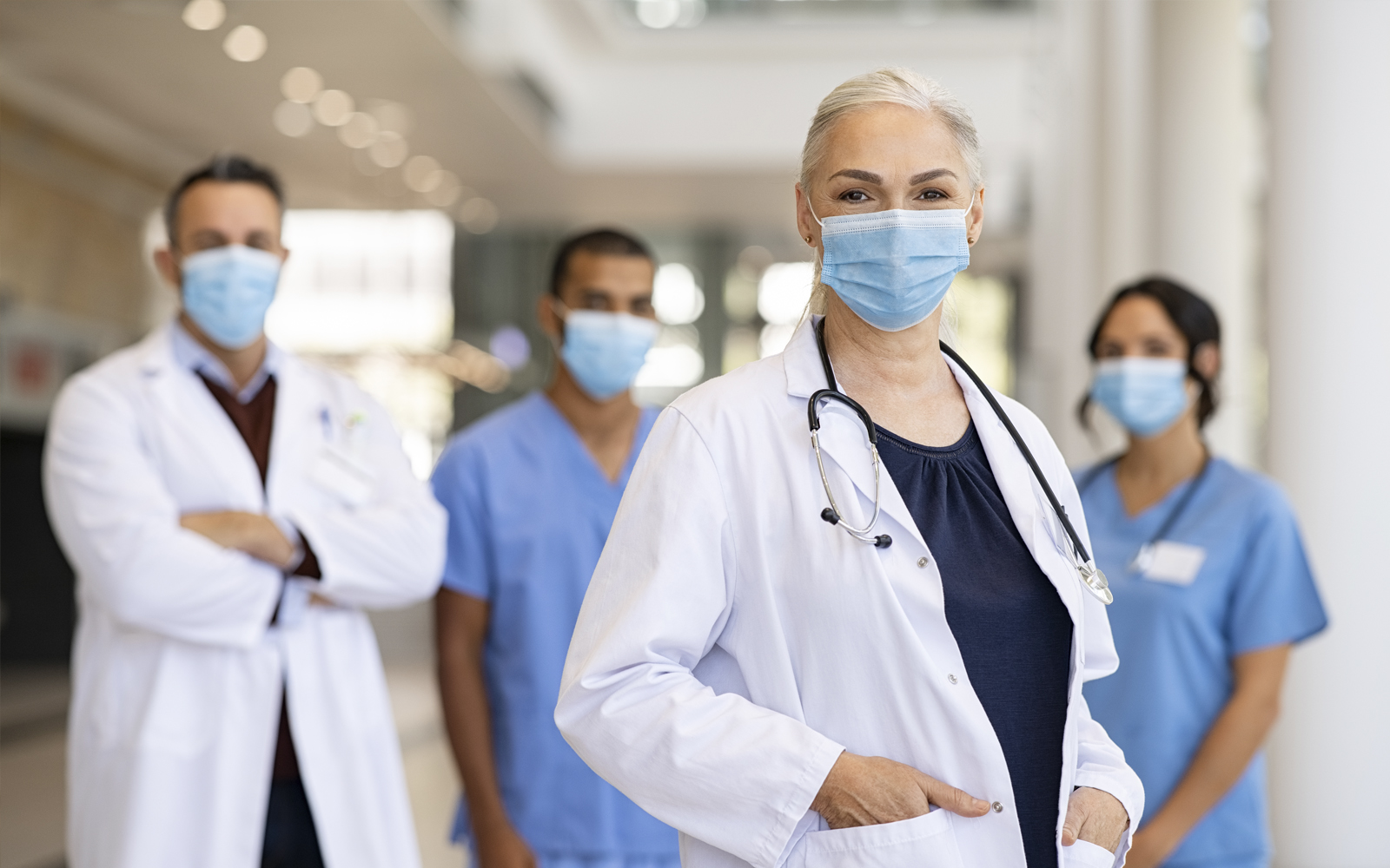Zwei Ärztinnen und Zwei Ärzte in Ihrer Arbeitskleidung und mit Schutzmaske lächeln in die Kamera