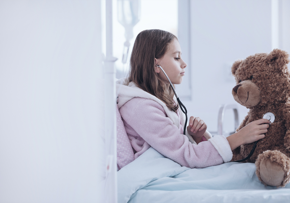 Mädchen in Krankenbett, welches Ihren Teddy mit einem Stethoskop abhört