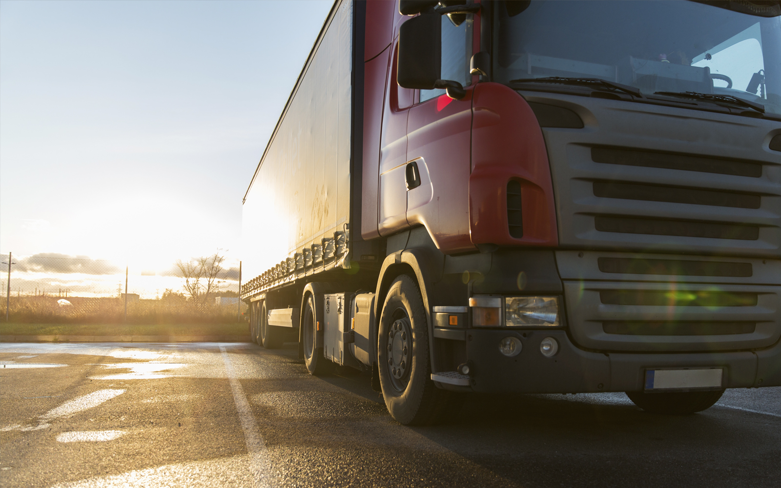 Roter LKW auf einem Parkplatzt, im Hintergrund ist ein Blauerhimmel und ein heller Sonnenschein