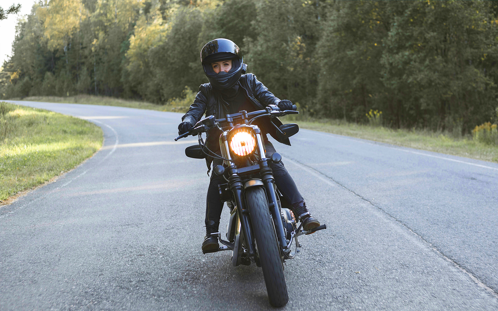 Frau fährt in schwarzer Motorradbekleidung und Helm mit einem schwarzen Motorrad auf einer Straße