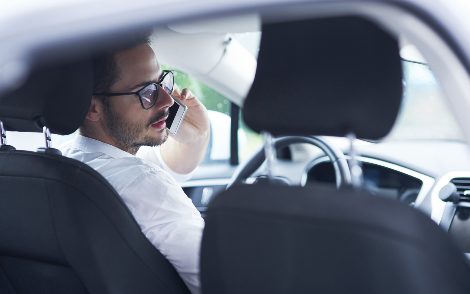Mann mit Hemnd und Brille sitzt in Auto und führt Telefonat