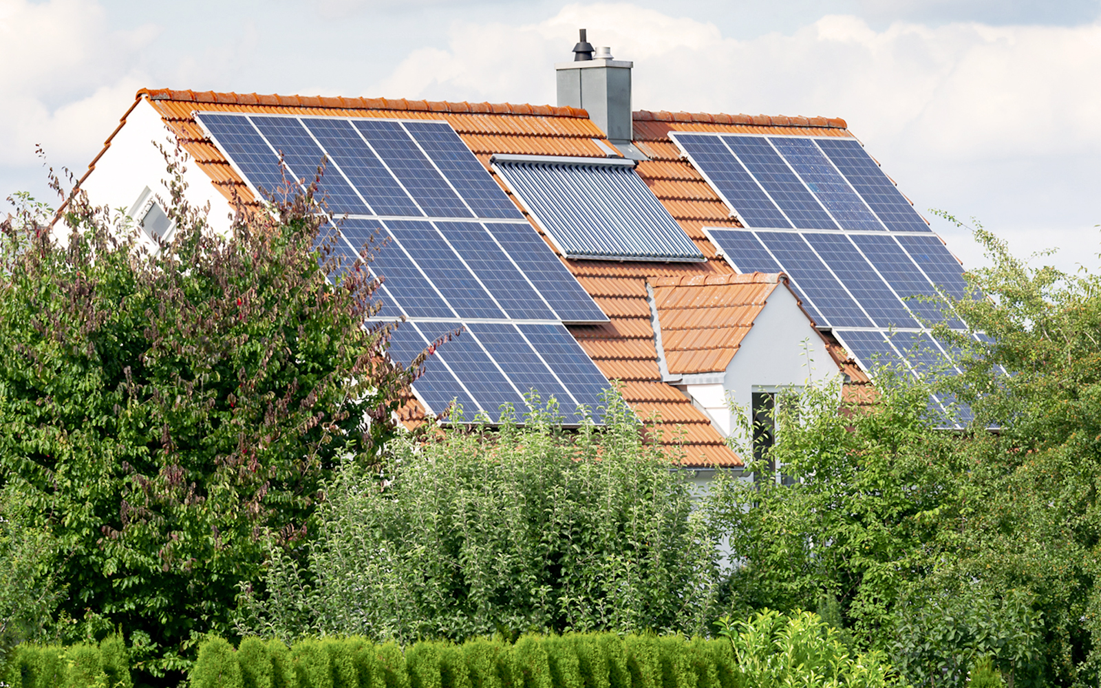 Hausdach inzwischen Sträuchern und Bäumen, auf welchem viele Solarzellen angebracht sind.
