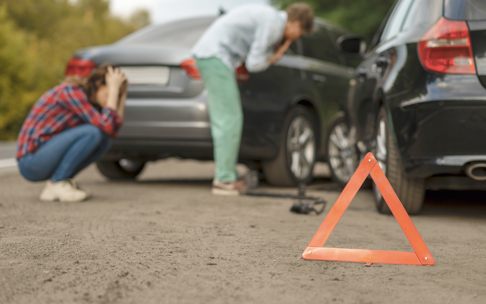 Warndreieck steht vorne rechts und im Hintergund sind zwei Frauen die einen Unfall miteinander hatten und sich die Autos verzweifelnd ansehen.