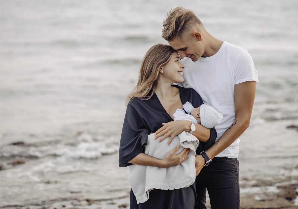 Junge Familie mit Baby kuschelnd an einem Strand