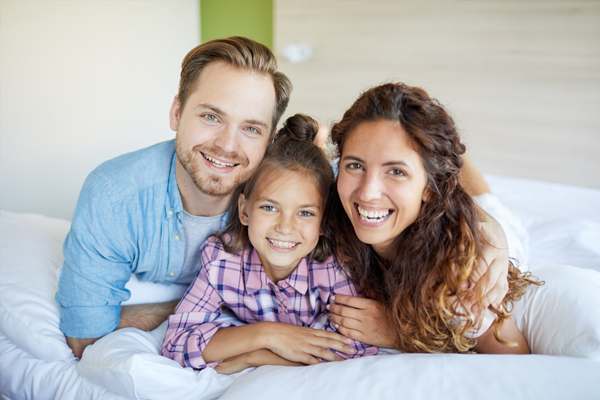 junge Familie kuschelt glücklich auf dem Bett